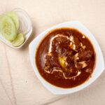 Top view of Indian kidney bean curry with cucumber, onions, and lime on the side.