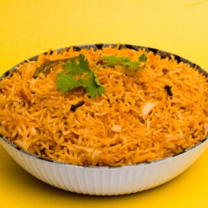 Aromatic Indian biriyani with spices served in a white bowl with a vibrant yellow background.
