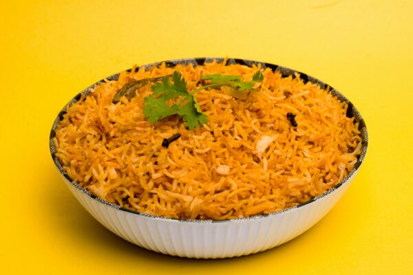 Aromatic Indian biriyani with spices served in a white bowl with a vibrant yellow background.