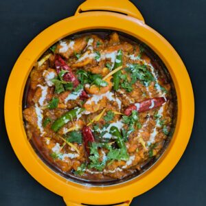 Top view of a flavorful Indian curry garnished with herbs and chilies, served in a vibrant dish.