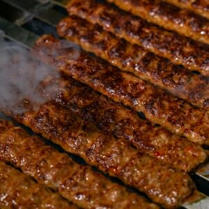 Close-up of sizzling spicy kebabs cooking on a charcoal grill with smoke rising.