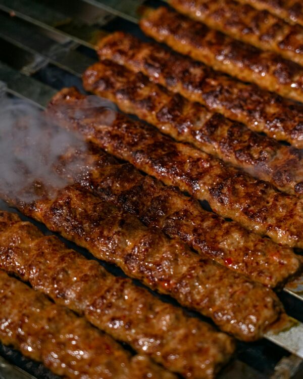 Close-up of sizzling spicy kebabs cooking on a charcoal grill with smoke rising.