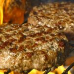 Close-up of juicy beef burgers grilling over open flames, perfect for summer BBQs.