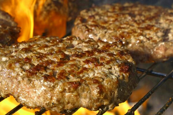 Close-up of juicy beef burgers grilling over open flames, perfect for summer BBQs.