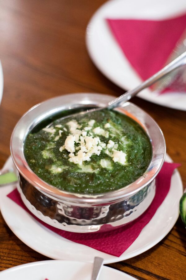 Top-down view of creamy palak paneer served in a stainless steel bowl, garnished with crumbled cheese.